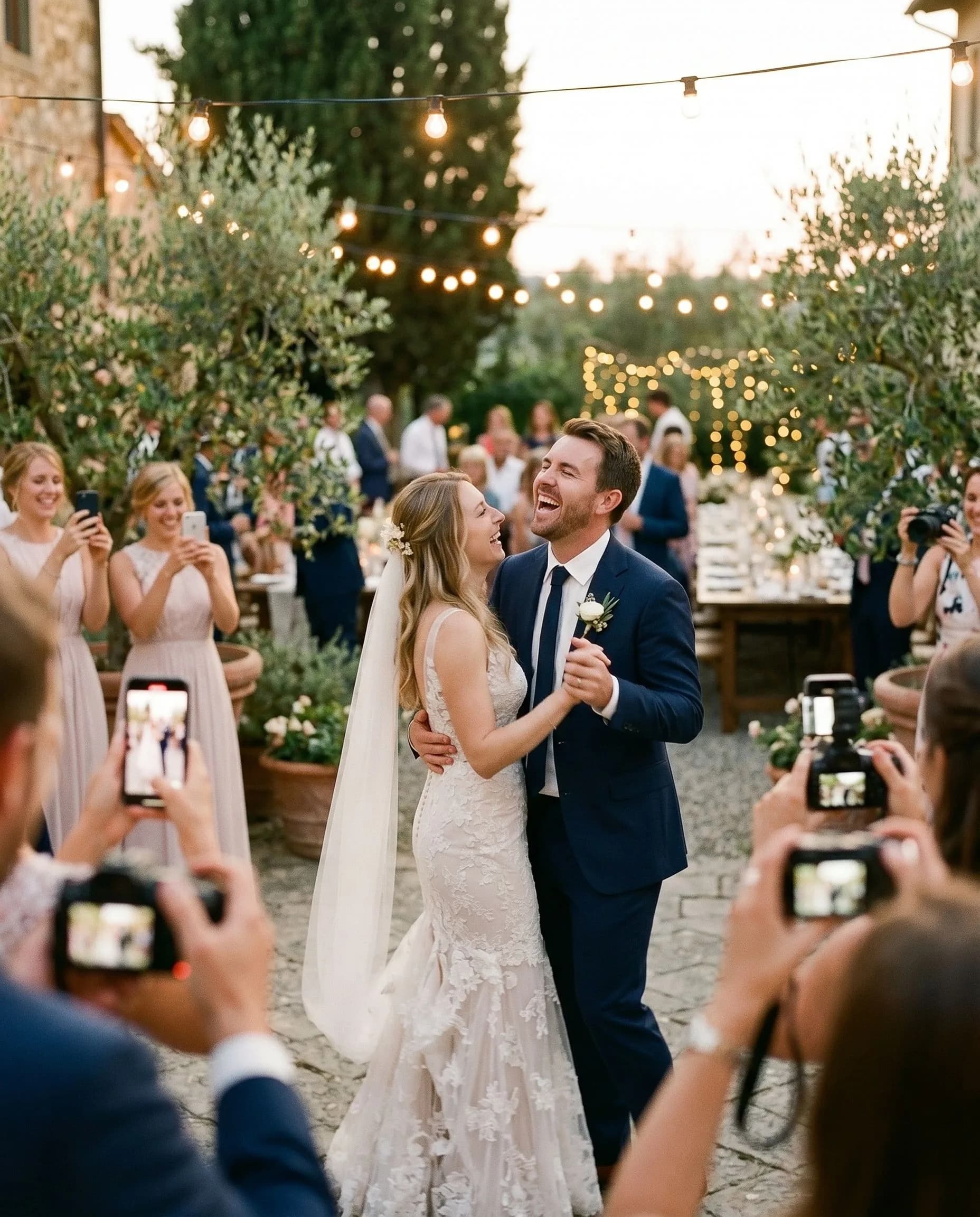 Newlyweds laughing mid-dance while wedding guests photograph them with their phones